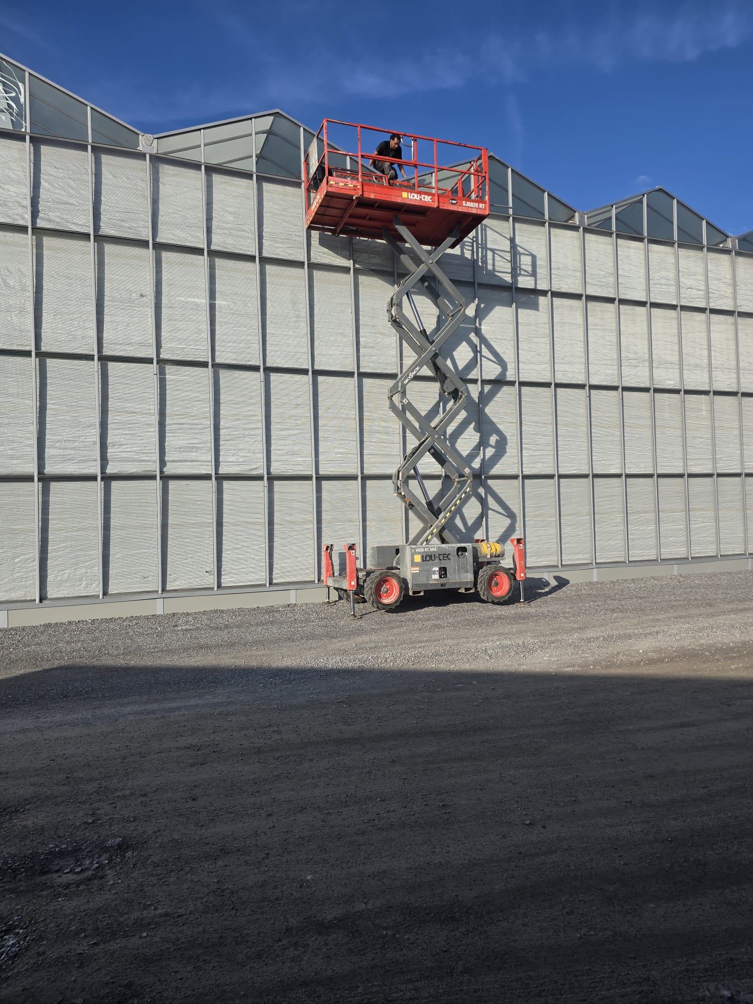 Scissor lift raised against greenhouse exterior wall