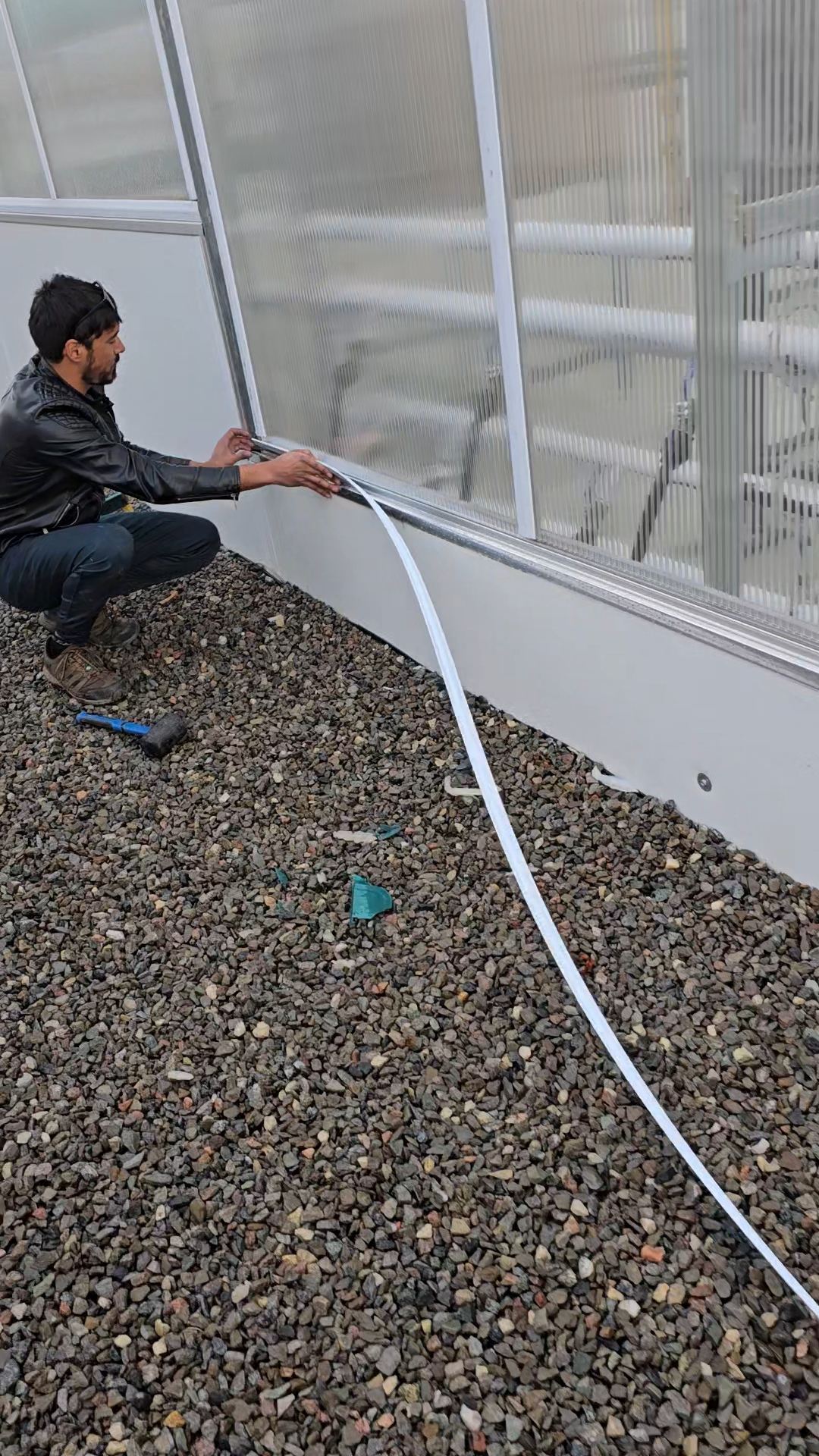 Technician installing polycarbonate edge trim on a greenhouse wall